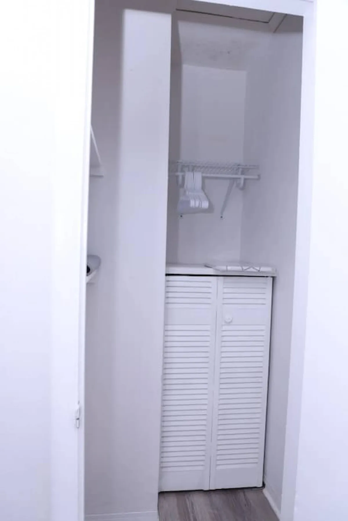A tidy closet with white louvered doors, a metal hanging rack with white hangers, and a compact but efficient layout. The space emphasizes organization and tidiness, contributing to an overall sense of comfort and order within the home environment.